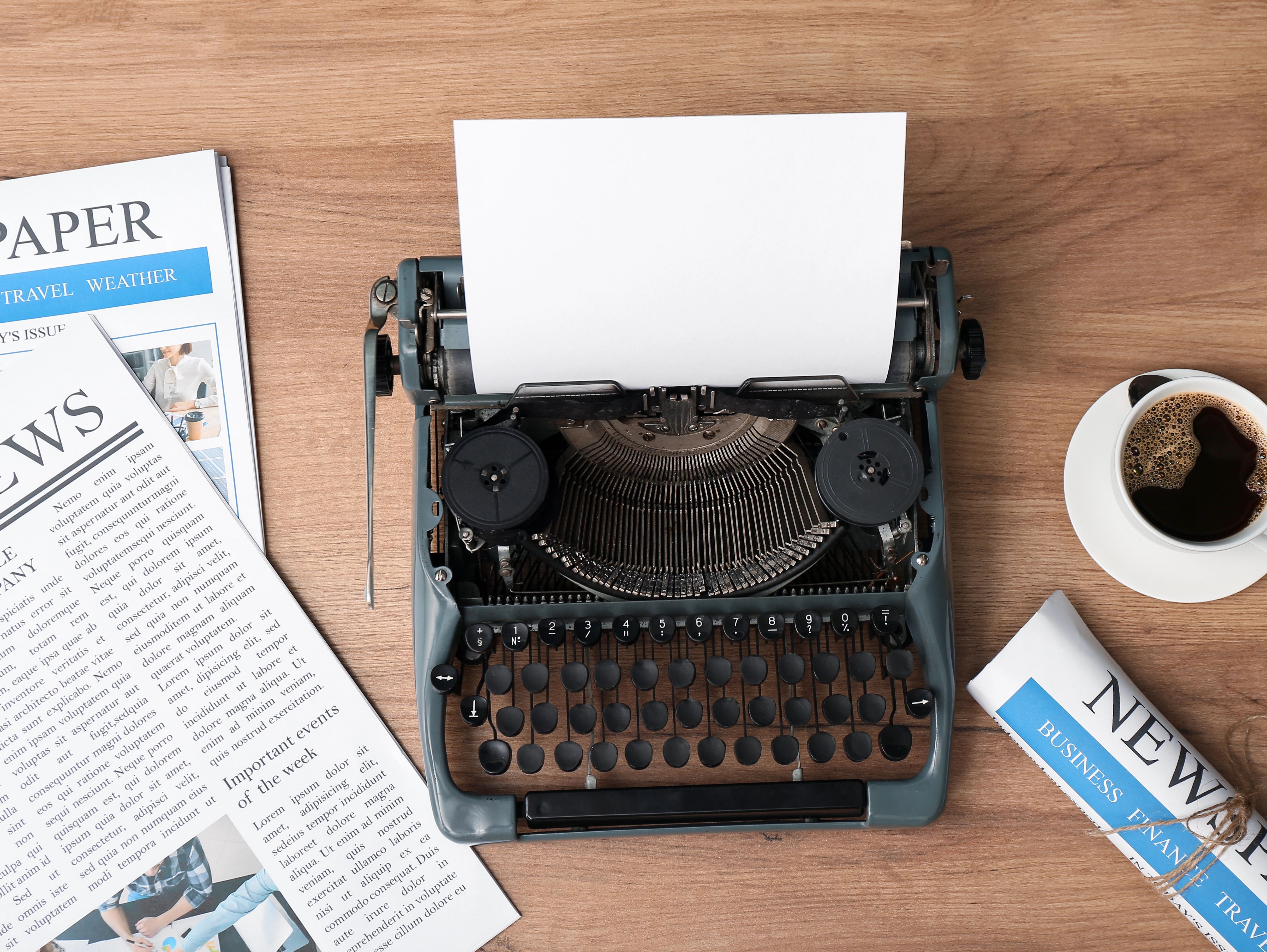 Das Bild zeigt eine Schreibmaschine, in die Papier gespannt ist. Daneben liegen mehrere englischsprachige Zeitungen.
