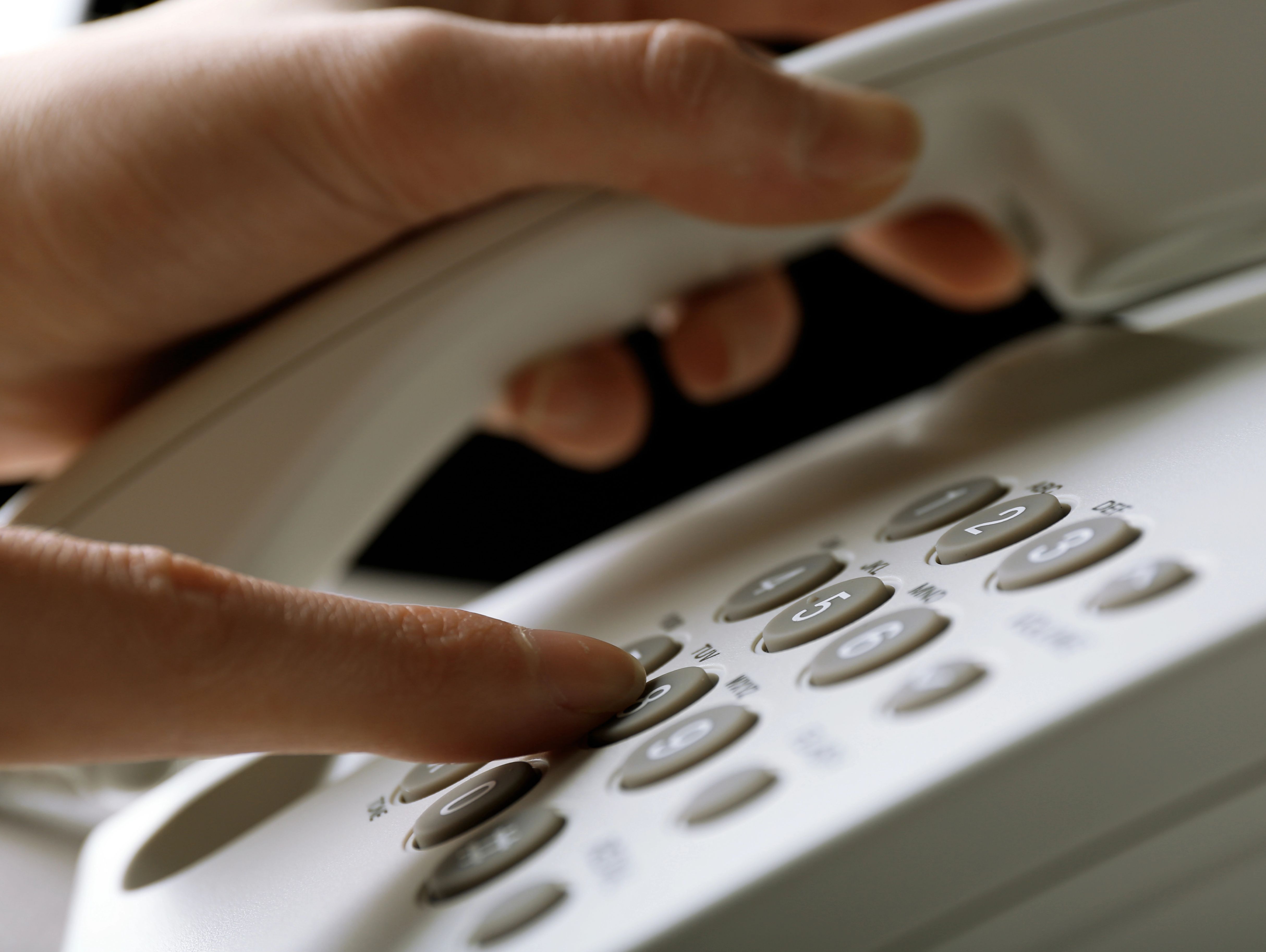 Das Bild zeigt ein Tastentelefon. Eine Hand hält den Hörer, die andere drückt eine Zifferntaste.